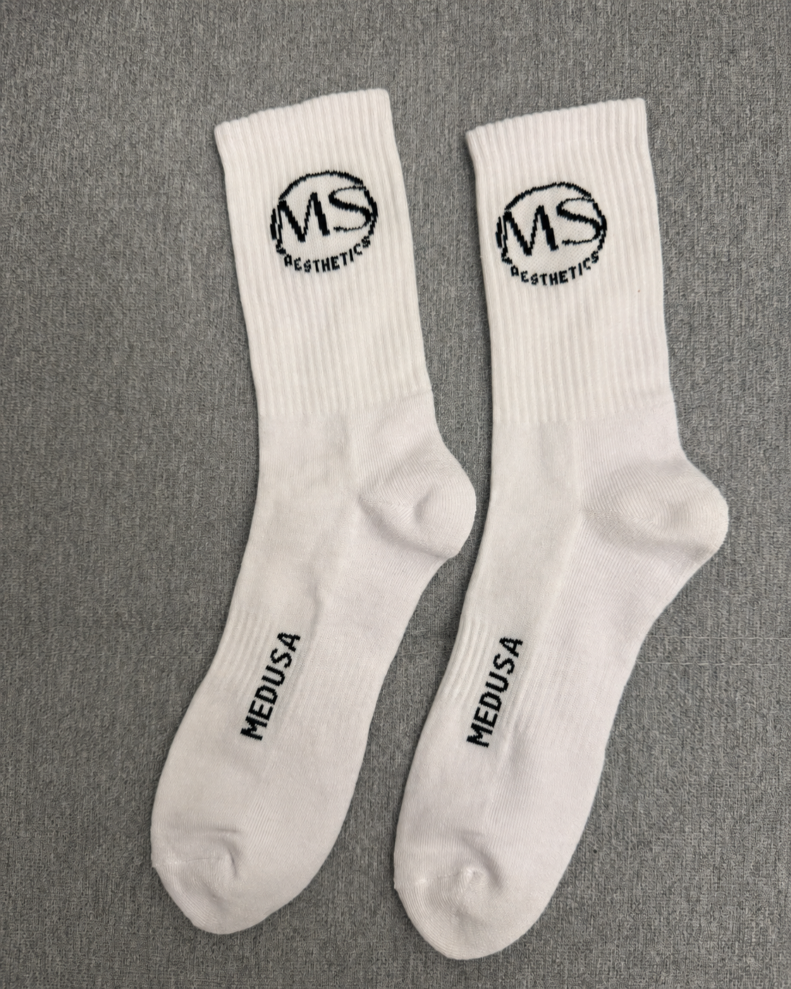 Physical white crew sock sample with MS Aesthetics cuff and MEDUSA foot branding